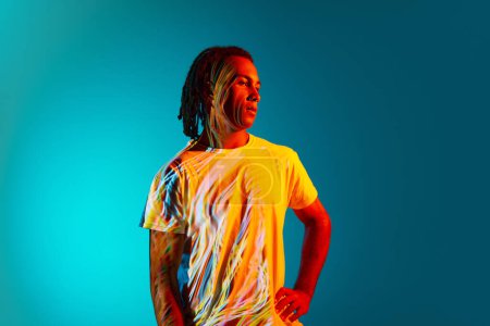 Photo for Portrait of young african man with dreads standing against blue, cyan background in neon light. Light reflection on body. Concept of art, fashion, modern style, cyberpunk, futurism, ad - Royalty Free Image