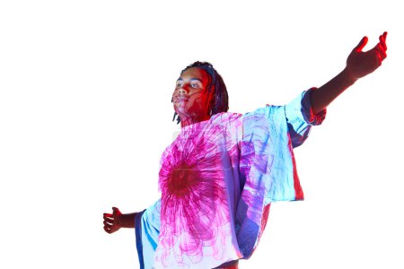 Foto de Sensaciones florecientes. Hombre africano joven guapo con reflejo de filtro colorido en el cuerpo posando sobre fondo blanco en luz de neón. Concepto de arte, moda, estilo moderno, cyberpunk, futurismo, anuncio - Imagen libre de derechos