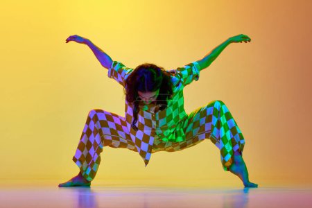 Téléchargez les photos : Performance contemp artistique. Jeune femme en vêtements élégants dansant sur fond jaune orange dégradé dans la lumière au néon. Concept de style de danse moderne, passe-temps, art, performance, style de vie, publicité - en image libre de droit