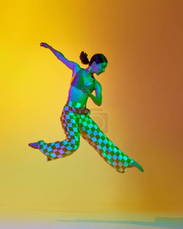 Photo for Artistic contemp performance. Young woman in stylish clothes dancing against gradient yellow orange background in neon light. Concept of modern dance style, hobby, art, performance, lifestyle, ad - Royalty Free Image