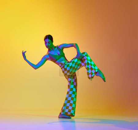 Téléchargez les photos : Jeune femme artistique talentueuse dansant contemporaine, danse freestyle sur fond jaune dégradé orange dans la lumière au néon. Concept de style de danse moderne, passe-temps, art, performance, style de vie, publicité - en image libre de droit
