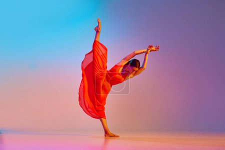 Foto de Imagen dinámica de joven talentosa, artista mujer en elegante vestido rojo bailando contra degradado fondo multicolor en luz de neón. Concepto de estilo de baile moderno, hobby, arte, performance, estilo de vida, anuncio - Imagen libre de derechos