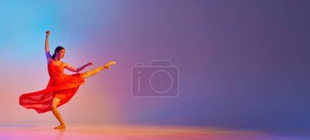 Téléchargez les photos : Elégante et talentueuse jeune femme en robe rouge longue dansant sur fond dégradé multicolore au néon. Concept de style de danse moderne, passe-temps, art, performance, style de vie, publicité. Bannière - en image libre de droit