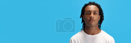 Foto de Retrato de un joven africano con rastas en camiseta blanca mirando a la cámara sobre fondo azul del estudio. Calma. Concepto de juventud, emociones humanas, estilo de vida, moda. Banner. Copiar espacio para anuncio - Imagen libre de derechos