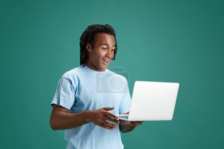 Foto de Jóvenes estudiantes mirando en el ordenador portátil con emoción y sonrisa en el fondo del estudio verde. Educación en línea. Concepto de juventud, emociones humanas, estilo de vida, moda, expresiones faciales, anuncio - Imagen libre de derechos