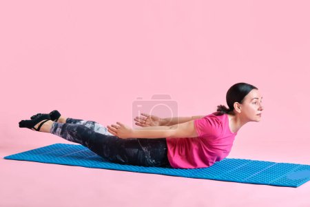 Téléchargez les photos : Forts exercices de dos. Femme mûre allongée sur un fitness mat et s'entraînant sur fond de studio rose. Concept de sport, mode de vie sain, fitness, soins du corps, bien-être, publicité - en image libre de droit