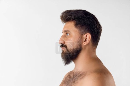 Photo for Side view of bearded man looking straight, posing shirtless against white studio background. Barber care. Concept of mens beauty, skin care, cosmetology, health and wellness. Copy space for ad - Royalty Free Image