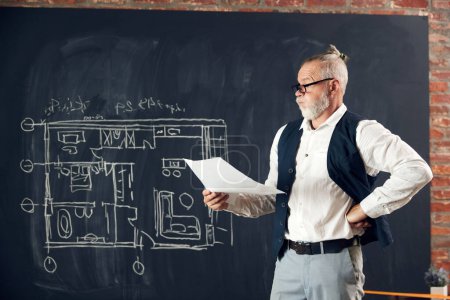 Photo for Senior man in stylish clothes looking on architectural design, drawings, sketches with thoughtful face, solving mistakes. Concept of profession, architecture, creation, occupation, business - Royalty Free Image