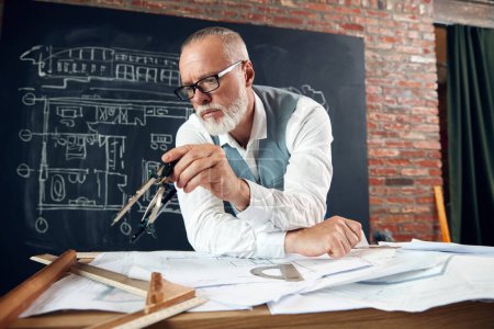 Photo for Bearded senior man, architect sitting at table and working with buildings design, sketches. Making measurements. Concept of profession, architecture, creation, occupation, business - Royalty Free Image