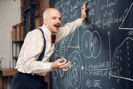Photo for Excited man, professor, scientist standing by blackboard with scientific formulas and calculations. Math, physics, chemistry lessons. Concept of education, science, profession, occupation, knowledge - Royalty Free Image