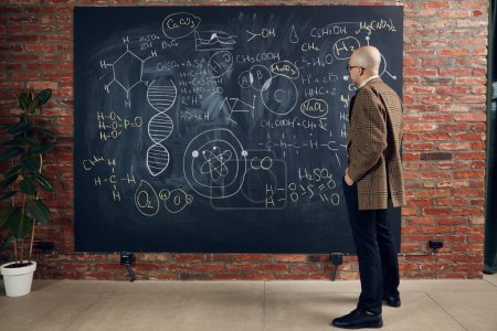 Photo for Young man, scientist standing by blackboard with formulas and calculations. Chemistry lessons. Concept of education, science, profession and occupation, knowledge - Royalty Free Image