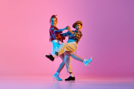 Photo for Beautiful, artistic, emotive children in retro stylish clothes dancing against pink studio background in neon light. Concept of childhood, hobby, active lifestyle, performance, art, fashion - Royalty Free Image