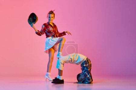 Photo for Flexibility. Stylish, active children, girl and boy in retro style clothes dancing over pink studio background in neon light. Concept of childhood, hobby, active lifestyle, performance, art, fashion - Royalty Free Image