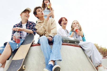 Photo for Cheerful, laughing, positive friends, teens sitting on skate park, ramp, talking, having fun and skateboarding. Youth culture, sport and dynamic, extreme, hobby and lesiure, friendship concept - Royalty Free Image