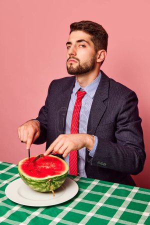 Photo for Serious man in a suit eating watermelon with knife and fork over pink background. Green checkered tablecloth. Concept of food, creativity, party, summer, health. Pop art photography. Copy space for ad - Royalty Free Image