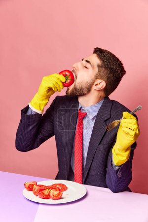 Foto de Empresario con guantes de goma comiendo tomates emocionalmente sobre fondo rosa. Concepto de comida, creatividad, fiesta, verano, salud. Fotografía de arte pop. Copiar espacio para anuncio - Imagen libre de derechos