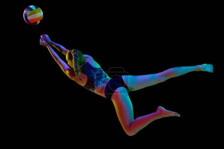 Photo for Dynamic image of young woman during game playing volleyball, hitting ball against black studio background in neon light. Concept of professional sport, competition, health, hobby, action, ad - Royalty Free Image