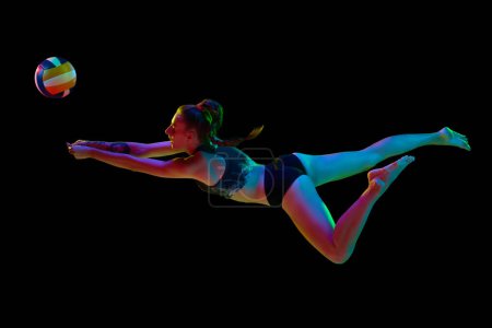 Photo for Young sportive woman, volleyball player hitting ball in motion and falling down against black studio background in neon light. Concept of professional sport, competition, health, hobby, action, ad - Royalty Free Image