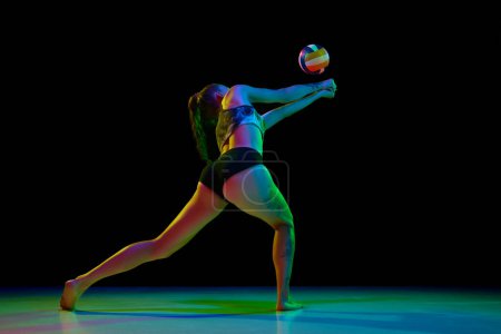 Foto de Jugadora profesional de voleibol femenino, mujer joven golpeando pelota contra fondo de estudio negro en luz de neón. Concentración. Concepto de deporte profesional, competición, salud, hobby, acción, anuncio - Imagen libre de derechos