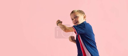 Foto de Retrato de niño juguetón, niño jugando, peleando, boxeando contra el fondo rosa del estudio. Concepto de infancia, emoción infantil, moda, estilo de vida positivo, diversión y alegría, anuncio - Imagen libre de derechos