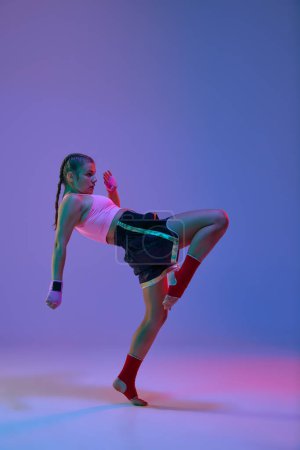 Photo for Full-length of sportive teen girl, mma fighter in uniform training against purple studio background in neon lights. Concept of mixed martial arts, sport, hobby, competition, athleticism, strength, ad - Royalty Free Image