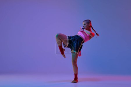 Photo for Dynamic photo of athletic teen girl, mma fighter in sportswear training against purple background in neon lights. Concept of mixed martial arts, sport, hobby, competition, athleticism, strength, ad - Royalty Free Image