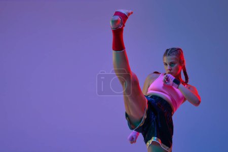 Photo for Leg kick. MMA fighter, teen girl training, fighting against purple studio background in neon lights. Concept of mixed martial arts, sport, hobby, competition, athleticism, strength, ad - Royalty Free Image