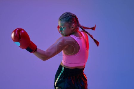 Photo for Sportive teen girl, MMA athlete in uniform and boxing gloves, training against purple background in neon lights. Concept of mixed martial arts, sport, hobby, competition, athleticism, strength, ad - Royalty Free Image