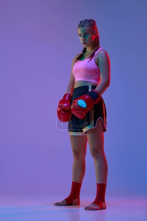 Photo for Full-length photo of serious teen girl in sportswear and boxing gloves, MMA fighter against purple background in neon lights. Concept of mixed martial arts, sport, hobby, winner, competition, ad - Royalty Free Image