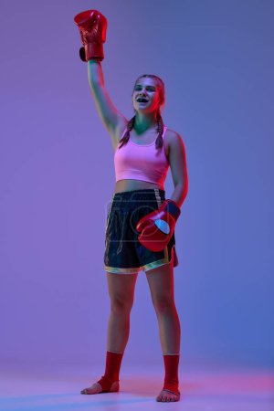 Photo for Full-length photo of teen girl in sportswear and boxing gloves, MMA fighter after winning game against purple background in neon lights. Concept of mixed martial arts, sport, hobby, competition, ad - Royalty Free Image