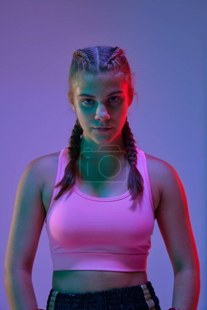 Photo for Portrait of sportive teen girl, athlete in sportswear, looking at camera against purple studio background in neon lights. Concept of mixed martial arts, sport, hobby, competition, strength, ad - Royalty Free Image