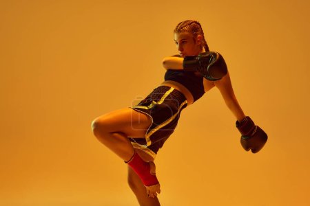 Photo for Dynamic photo of athletic teen girl, mma fighter in sportswear training against orange background in neon lights. Concept of mixed martial arts, sport, hobby, competition, athleticism, strength, ad - Royalty Free Image
