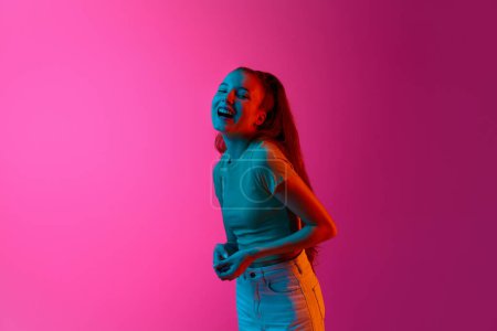 Photo for Portrait of beautiful young girl cheerfully laughing against pink studio background in neon light. Happiness. Concept of human emotions, fashion, beauty, lifestyle, youth, ad - Royalty Free Image