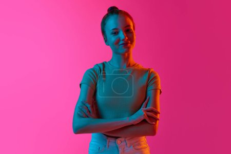 Téléchargez les photos : Belle jeune fille avec un chignon, souriant, regardant tendrement la caméra sur fond de studio rose dans la lumière du néon. Concept d'émotions humaines, mode, beauté, mode de vie, jeunesse, publicité - en image libre de droit