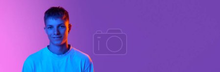 Photo for Handsome young guy with cute smile looking at camera against gradient pink purple background in neon light. Concept of human emotions, youth, lifestyle, facial expressions. Banner. Copy space for ad - Royalty Free Image