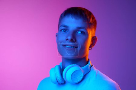 Foto de Retrato de joven guapo en auriculares contra el color rosa degradado fondo púrpura en luz de neón. Concepto de emociones humanas, juventud, estilo de vida, moda, expresiones faciales, anuncio - Imagen libre de derechos