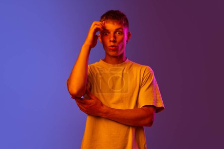 Photo for Young guy in white t-shirt standing with shocked face against gradient purple background in neon light. Concept of human emotions, youth, lifestyle, fashion, facial expressions, ad - Royalty Free Image
