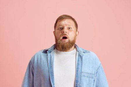 Photo for Bearded man in casual clothes standing with wide open eyes and mouth, showing shocked face over pink studio background. Concept of human emotions, lifestyle, facial expression, ad. Copy space for ad - Royalty Free Image