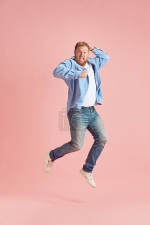 Photo for Full-length image of bearded mature man in casual clothes emotionally jumping and shouting over pink studio background. Concept of human emotions, lifestyle, facial expression, ad. Copy space for ad - Royalty Free Image