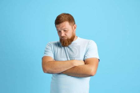 Téléchargez les photos : Homme barbu rousse debout avec un visage triste et réfléchi sur fond de studio bleu. Concept d'émotions humaines, mode de vie, expression faciale, annonce. Espace de copie pour la publicité - en image libre de droit