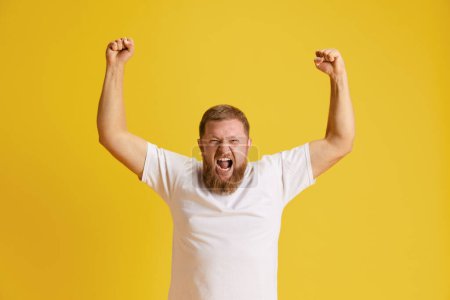 Photo for Bearded man, sport fun feeling happy and excited, raising hand up against yellow studio background. Success. Concept of human emotions, lifestyle, facial expression, ad. Copy space for ad - Royalty Free Image