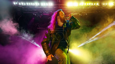 Photo for Rock and roll concert. Artistic, expressive man with long hair, in leather clothes making performance, emotionally singing. Music, performance, art, talent, nightlife, joy, party and lifestyle concept - Royalty Free Image