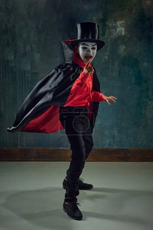 Téléchargez les photos : Petit garçon, enfant à l'image d'un vampire effrayant vêtu d'un costume et maquillé sur un fond vintage sombre. Horreur. Concept d'Halloween, enfance, célébration, fête, vacances, créativité, annonce - en image libre de droit