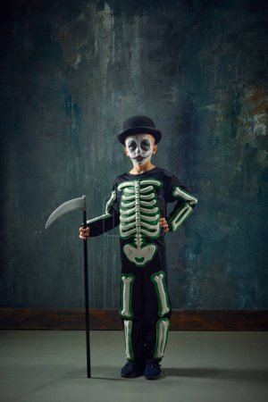 Photo for Little boy, child with pale face makeup, wearing costume of skeleton, standing with scythe over vintage green background. Concept of Halloween, childhood, celebration, party, holiday, creativity, ad - Royalty Free Image