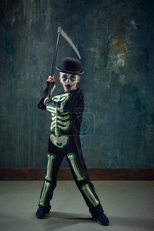 Photo for Fantasy. Little boy, child with pale face makeup, wearing costume of skeleton, standing with scythe over vintage green background. Concept of Halloween, childhood, celebration, holiday, creativity, ad - Royalty Free Image