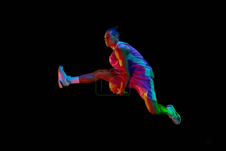 Photo for Competitive teen boy in motion, playing, training basketball, jumping with ball against black studio background in neon light. Concept of professional sport, competition, hobby, game, competition - Royalty Free Image