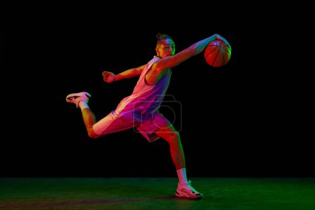 Photo for Muscular, active young man in motion, basketball player with ball during game against black background in neon light. Concept of professional sport, competition, hobby, active lifestyle, competition - Royalty Free Image