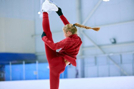 Photo for Twine. Flexible and artistic girl, figure skating athlete in red sportswear training, doing exercises on ice rink arena. Concept of professional sport, competition, sport school, health, hobby, ad - Royalty Free Image