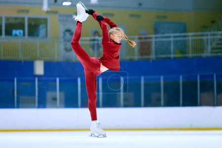 Foto de Chica talentosa y flexible en movimiento, atleta de patinaje artístico en entrenamiento de ropa deportiva roja en pista de hielo arena. Preparación del campeonato. Concepto de deporte profesional, competición, escuela de deporte, hobby, anuncio - Imagen libre de derechos