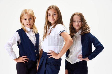 Photo for Beautiful children, girls, friends wearing school uniform, standing against white studio background. Classmates. Concept of childhood, school, education, fashion, style. Copy space for ad - Royalty Free Image